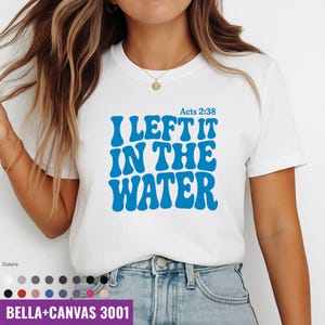 Op de afbeelding: Wit T-shirt met de tekst "I LEFT IT IN THE WATER" in blauw, met "Acts 2:38" erboven. Het shirt is een Bella+Canvas 3001, met een verscheidenheid aan kleuropties eronder.