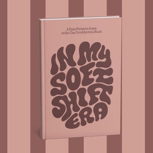 May include: A hardcover book with a light pink cover and the title "IN MY SOFT SHIFT ERA" in brown, stylized lettering. The book also features the text "A Queer Postpartum Journal for Self-Care, Faith & Emotional Healing."