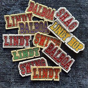 May include: A collection of ten felt patches with various names and words, including "Lindy", "Balboa", "Shag", and "Swing". The patches are in various colors, including red, yellow, green, and purple.