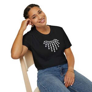 May include: A black t-shirt with a white graphic of a necklace with a pendant. The necklace is a symbol of justice.