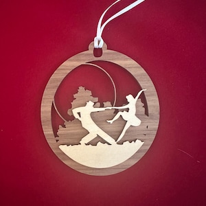 May include: A wooden ornament featuring a silhouette of two dancers in a ballroom pose. The ornament is oval shaped and has a white ribbon for hanging.