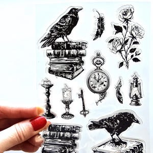 Peut inclure: Feuille d'autocollants transparente avec des illustrations en noir et blanc. Comprend un corbeau sur des livres, des roses, une montre de poche, des plumes, des bougies, une clé et une lanterne. Les illustrations ont une esthétique gothique vintage.