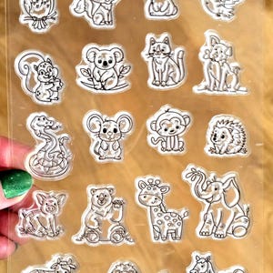 以下が含まれることがあります： 動物をテーマにしたスタンプの透明なシート。フクロウ、キツネ、ウサギ、リス、コアラ、猫、犬、ヘビ、ネズミ、サル、ハリネズミ、豚、クマ、キリン、ゾウ、ウシ、ライオン、ウマなど、さまざまな動物が描かれています。