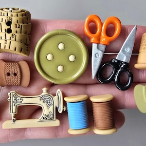 Peut inclure: Collection de boutons sur le thème de la couture. Comprend un mètre ruban, des dés à coudre, des bobines de fil, une machine à coudre, des ciseaux et un gros bouton vert avec quatre petits boutons blancs.