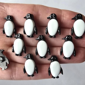 Peut inclure: Collection d'ornements en forme de petits pingouins. Chaque pingouin a une tête et des ailes noires, un ventre blanc et de petits pieds noirs. Un pingouin a une attache métallique au dos.