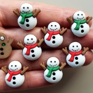 以下が含まれることがあります： 赤と緑のスカーフと茶色の小枝の腕が付いた白い雪だるまのボタン8個の詰め合わせ。