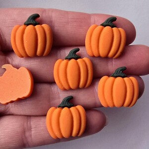May include: Six small orange pumpkin-shaped decorations with green stalks. One pumpkin is cut in half. The pumpkins are a bright orange colour, ideal for autumn-themed crafts and decorations.