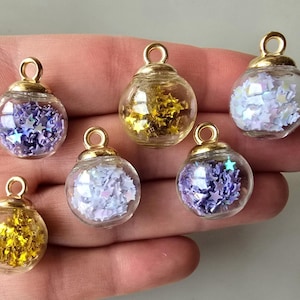 May include: Six gold-toned pendant charms with clear glass globes filled with iridescent star-shaped glitter. The glitter is in shades of purple, blue, and white.