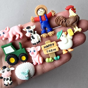 May include: A collection of small, colourful farm-themed buttons featuring a scarecrow, a rooster, two pigs, two cows, a green tractor, a white sheep, a duck wearing a hat, and a tan sign with the text HAPPY FARM printed in black letters.