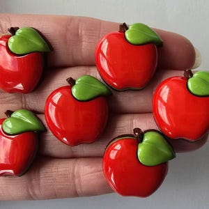May include: Six red apple-shaped buttons with green leaves. The buttons are glossy and have a 3D effect.