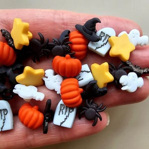 以下が含まれることがあります： ハロウィンをテーマにしたボタンのコレクションで、かぼちゃ、幽霊、クモ、墓石、星など、さまざまなデザインが施されています。ボタンはプラスチック製で、オレンジ、ブラック、ホワイト、イエローなど、さまざまな色があります。