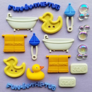 May include: A set of 12 colourful bath-themed buttons featuring a yellow rubber duck, a white bathtub, a blue sailboat, a yellow towel with the text "Bath Time", and two white bars of soap with the text "Soap". The buttons are decorated with iridescent bubbles and the text "Fun in the Tub".