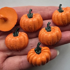 May include: A selection of orange pumpkin-shaped embellishments with green stems. One pumpkin button is also included. These miniature pumpkins are ideal for autumn-themed crafts and decorations.