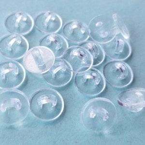 May include: A group of clear plastic buttons with a silver metal loop on each button.
