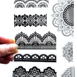 May include: Black lace border and mandala designs on clear plastic sheets. The designs include floral, heart, and geometric patterns. A hand holds a sheet with several designs, showcasing the intricate details.