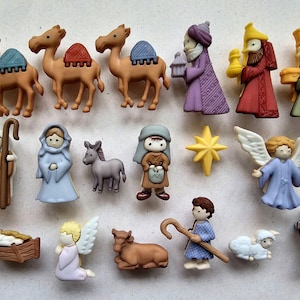 May include: A set of 16 colourful Christmas buttons featuring a nativity scene with three wise men, a donkey, a camel, a sheep, an angel, a star, and a manger. The buttons are made of plastic and have a variety of textures and designs.