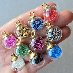 May include: A collection of ten small, spherical glass charms, each topped with a gold-toned metal cap and loop. The hollow glass globes are filled with tiny, colourful micro-beads in shades of red, blue, gold, pink, green, white, black, and silver.