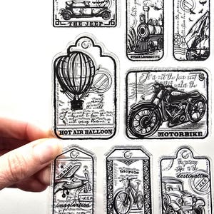 May include: A sheet of clear stickers with black and white illustrations of vintage vehicles and travel themes. Designs include a jeep, steam locomotive, sailboat, hot air balloon, motorbike, airplane, bicycle, and classic car. Text includes "THE JEEP", "STEAM LOCOMOTIVE", "HOT AIR BALLOON", "MOTORBIKE".