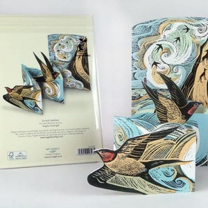 May include: Greeting cards with a pop-up swallow design. The cards feature a detailed illustration of swallows in flight, with a backdrop of swirling blue and tan patterns. The text "Cornish Swallows" is visible on the packaging.