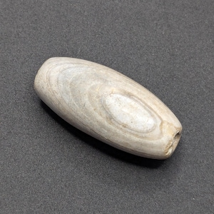 May include: A smooth, oval-shaped, light gray stone bead with a hole drilled through it. The bead has a natural, swirling pattern.