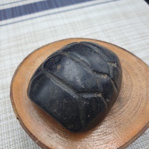 May include: A black, carved stone sphere with a geometric pattern. The sphere is resting on a wooden surface.