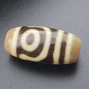 Könnte beinhalten: Eine braune und weiße Achatperle mit einem wirbelnden Muster. Die Perle ist oval geformt und hat eine glatte, polierte Oberfläche.