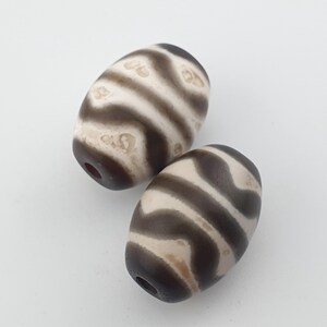 May include: Two oval-shaped beads with a white and brown striped pattern. The beads are made of a smooth, polished material.
