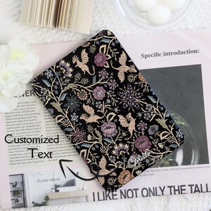 May include: Black tablet case with a floral and dragon design. The case features a repeating pattern of flowers, leaves, and dragons in shades of purple, beige, and green. The word "Coral" is written on the case.