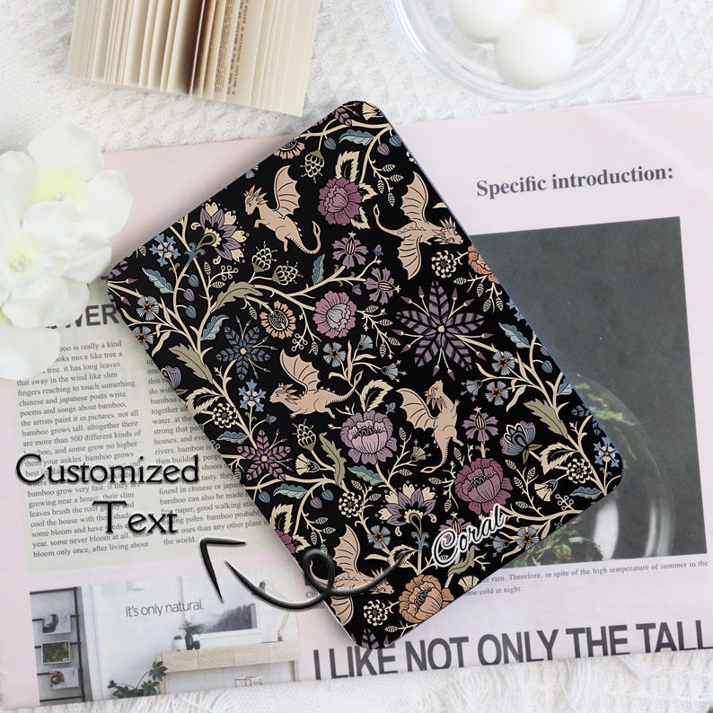 May include: Black tablet case with a floral and dragon design. The case features a repeating pattern of flowers, leaves, and dragons in shades of purple, beige, and green. The word "Coral" is written on the case.
