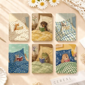 May include: A set of six rectangular notebooks featuring illustrations of animals reading books in bed. The designs include a cat, a dachshund, a French bulldog, a tabby cat, a frog, and a capybara, each tucked under patterned blankets.