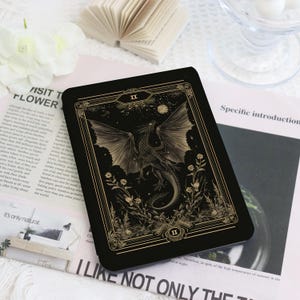 May include: A black rectangular card featuring a detailed illustration of a dragon with outstretched wings, surrounded by flowers and foliage. The card has a gold border and the Roman numeral "II". The background is dark.