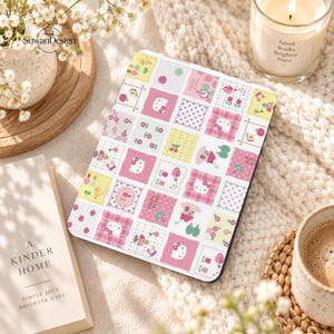 Peut inclure: Une housse de liseuse rectangulaire avec un motif patchwork composé de carrés roses, blancs et jaunes. Le design présente des illustrations de Hello Kitty, des petites fleurs, des pois, des cerises, des pommes et des arrosoirs en grille.