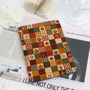 May include: A rectangular e-reader cover featuring a patchwork design of autumn-themed squares. The pattern includes orange pumpkins, brown coffee mugs with hearts, red and gold maple leaves, and various plaid, polka dot, and knit textures.