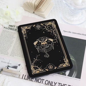 May include: A black e-reader cover featuring a gold-colored line art illustration of a dragon centered within a circular frame. The design includes intricate gold floral borders, celestial motifs, and a small circular emblem at the bottom center.