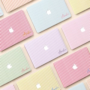 May include: A collection of laptop skins featuring vertical stripes in various pastel colors including pink, blue, green, yellow, and purple. Each skin displays a central white Apple logo cutout and the name Amelia written in a cursive script font.
