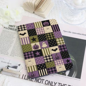 Può includere: Una custodia rettangolare per e-reader con un design patchwork di quadrati viola, verde oliva e crema. Il motivo include illustrazioni di zucche, fantasmi, pipistrelli, stelle e varie stampe geometriche come strisce, pois e motivi a quadri.