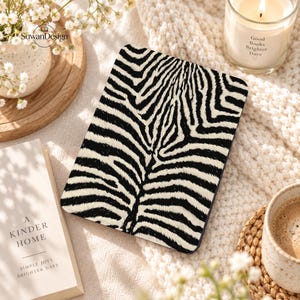May include: A rectangular e-reader device featuring a high-contrast black and white zebra stripe pattern across its front surface. The device has rounded corners and a smooth, flat display area, showcasing a bold animal print design.