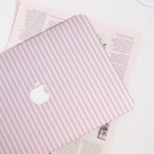 May include: A pink and white striped laptop cover with the Apple logo. The cover is on top of a pink paper with text. The background is a white surface.