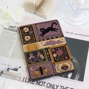 Può includere: Una custodia rettangolare per e-reader con un'illustrazione a più pannelli raffigurante un gatto nero, un sole, nuvole viola, composizioni floreali, boccette di pozioni, una falena e un cuore, con una palette di colori viola, oro e nero.