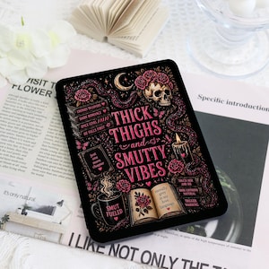 May include: A black rectangular e-reader skin featuring a pink graphic design with a skull, roses, a stack of books, a burning candle, and a coffee mug. The text reads Thick Thighs and Smutty Vibes, along with book-related phrases and labels.