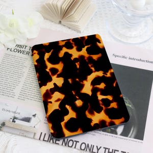 May include: A rectangular, tortoiseshell-patterned object with a glossy finish. The design features a mix of dark brown and amber tones, creating a marbled effect. The object is placed on a white surface with printed materials.