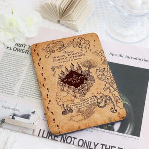 May include: A rectangular e-reader cover featuring a tan, parchment-style design with the Marauder's Map illustration. It displays the text 'Messrs. Moony, Wormtail, Padfoot & Prongs are proud to present The Marauders Map' and 'I solemnly swear that I am up to no good'.