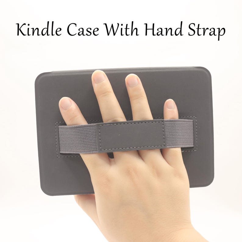 May include: A dark gray Kindle case with a hand strap. The case is rectangular and features a gray elastic hand strap for secure holding. The text "Kindle Case With Hand Strap" is displayed at the top.