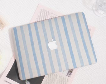 Może przedstawiać: Laptop z jasnoniebieskim i białym wzorem w paski. Logo Apple jest widoczne na środku. Laptop leży na różowej gazecie z tekstem.