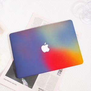 May include: A laptop skin featuring a vibrant, multi-coloured gradient design that transitions from deep blue and purple on the left to bright red, orange, and yellow on the right, with a central white Apple logo cutout visible on the surface.