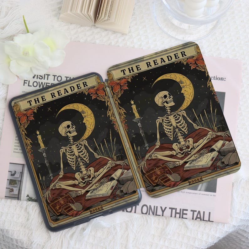 K&ouml;nnte beinhalten: Zwei Handyh&uuml;llen mit einem Tarotkarten-Design. Jede H&uuml;lle zeigt ein Skelett, einen Mond und Kerzen vor einem dunklen Hintergrund. Der Text "THE READER" steht oben. Die H&uuml;llen liegen auf einer hellrosa Oberfl&auml;che.