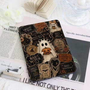 May include: A rectangular e-reader cover featuring a collage of Halloween-themed illustrations including a ghost holding a pumpkin, a black cat in a witch hat, a skeleton hand, and text such as "100% That Witch," "Bad Witch Club," and "Stay Creepy."