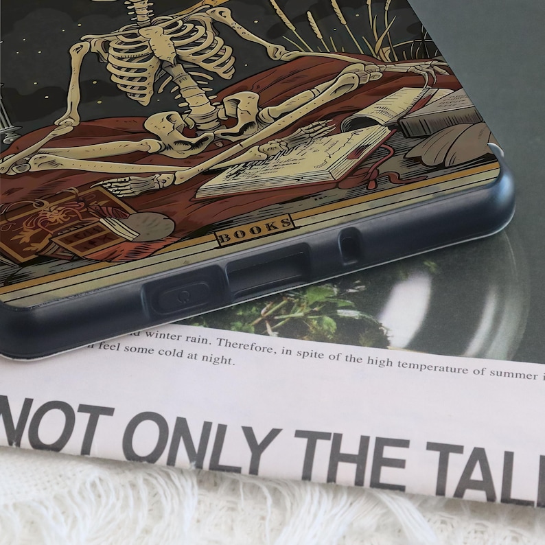 K&ouml;nnte beinhalten: Schwarze Handyh&uuml;lle mit einer detaillierten Illustration eines Skeletts, das sich auf einem Bett mit B&uuml;chern ausruht. Das Design enth&auml;lt das Wort "BOOKS" und eine dunkle, gotische &Auml;sthetik. Die H&uuml;lle besteht aus strapazierf&auml;higem Kunststoff.