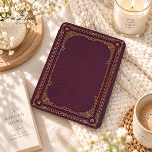 May include: A rectangular e-reader case in a deep plum purple color with a textured surface. The case features an intricate gold-colored border with ornate filigree patterns and geometric corner accents, framing the solid purple center.