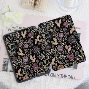 May include: Two black tablet cases with a floral and dragon pattern. The design features dragons, flowers, and foliage in shades of beige, purple, and green against a black background. The cases are on a light pink surface.